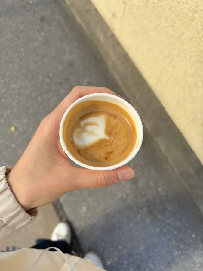 Kaffee zum Mitnehmen mit Latte Art in der Hand, auf dem Gehsteig