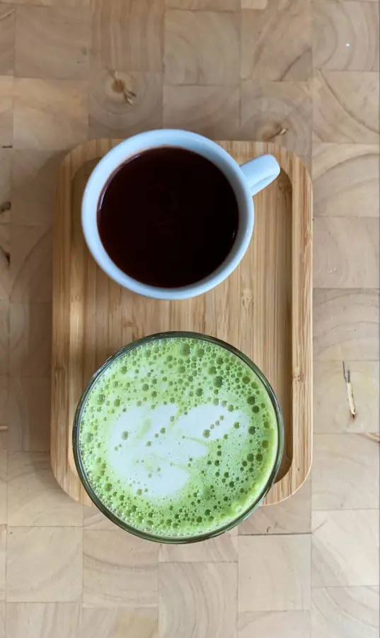 Schwarzer Kaffee und Matcha Latte mit Latte Art auf einem Holztablett, von oben