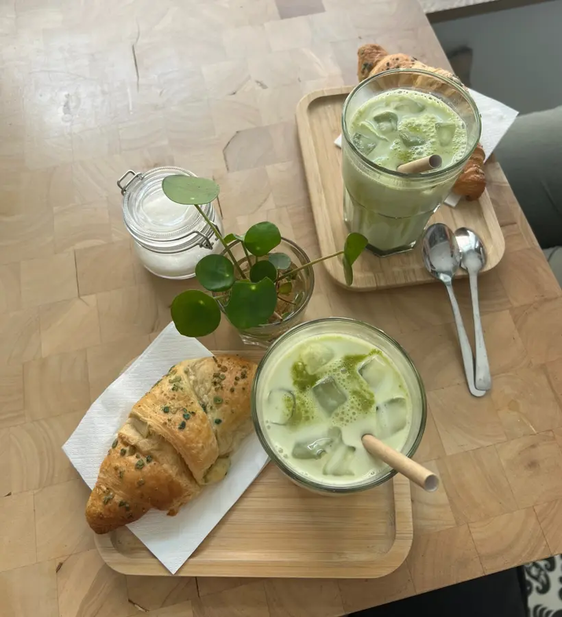 Iced Matcha Latte mit Croissant und einer kleinen Pflanze auf dem Tisch